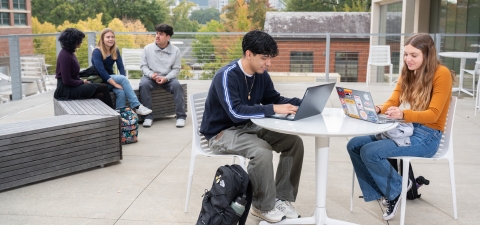 Students sitting at outdoor table working on laptops
