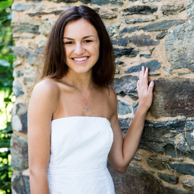 Cecilia's grad photo posing in a white dress in front of a stone wall 
