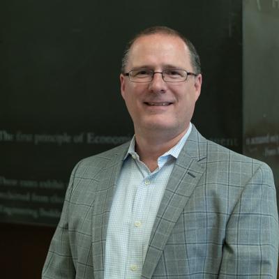 Danny Hughes professional headshot in front of classroom chalkboard