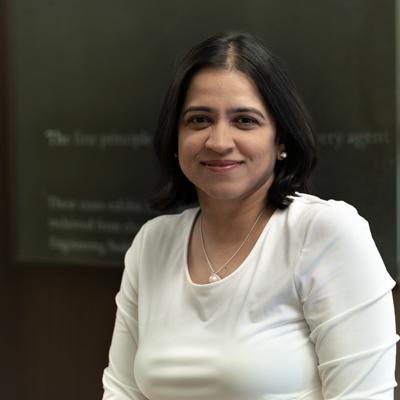 Headshot of associate professor Shatakshee Dhongde in front of a chalkboard