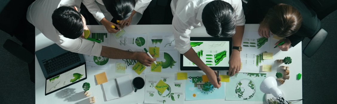 A group of individuals collaborating on a project, surrounded by green paper and brainstorming ideas.